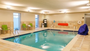 An indoor swimming pool with clear water, green chairs, a lifeguard stand, and a towel rack. - Hampton Inn & Suites New Albany Columbus (New Albany)