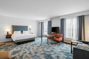 A hotel room with a bed, a desk, a chair, a TV, and a window with curtains.