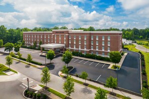 A large brick building with a central entrance and multiple windows, surrounded by a parking lot and greenery. - Hampton Inn & Suites New Albany Columbus (New Albany)