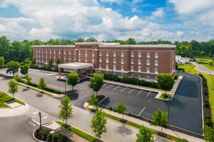 A large brick building with a central entrance and multiple windows, surrounded by a parking lot and greenery.