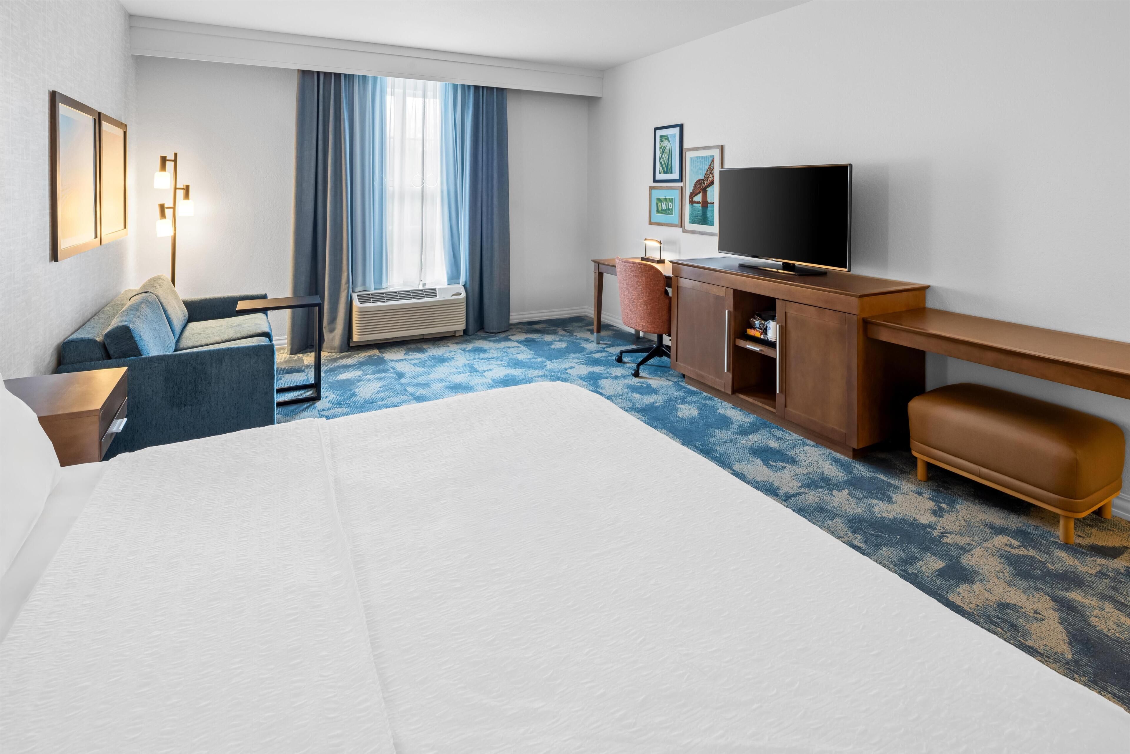 Een hotelkamer met een groot bed, een bureau, een stoel, een televisie en een raam met gordijnen.