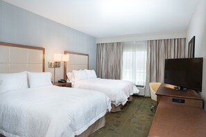 Et hotelværelse med to senge, et fjernsyn, et skrivebord og et vindue med gardiner.