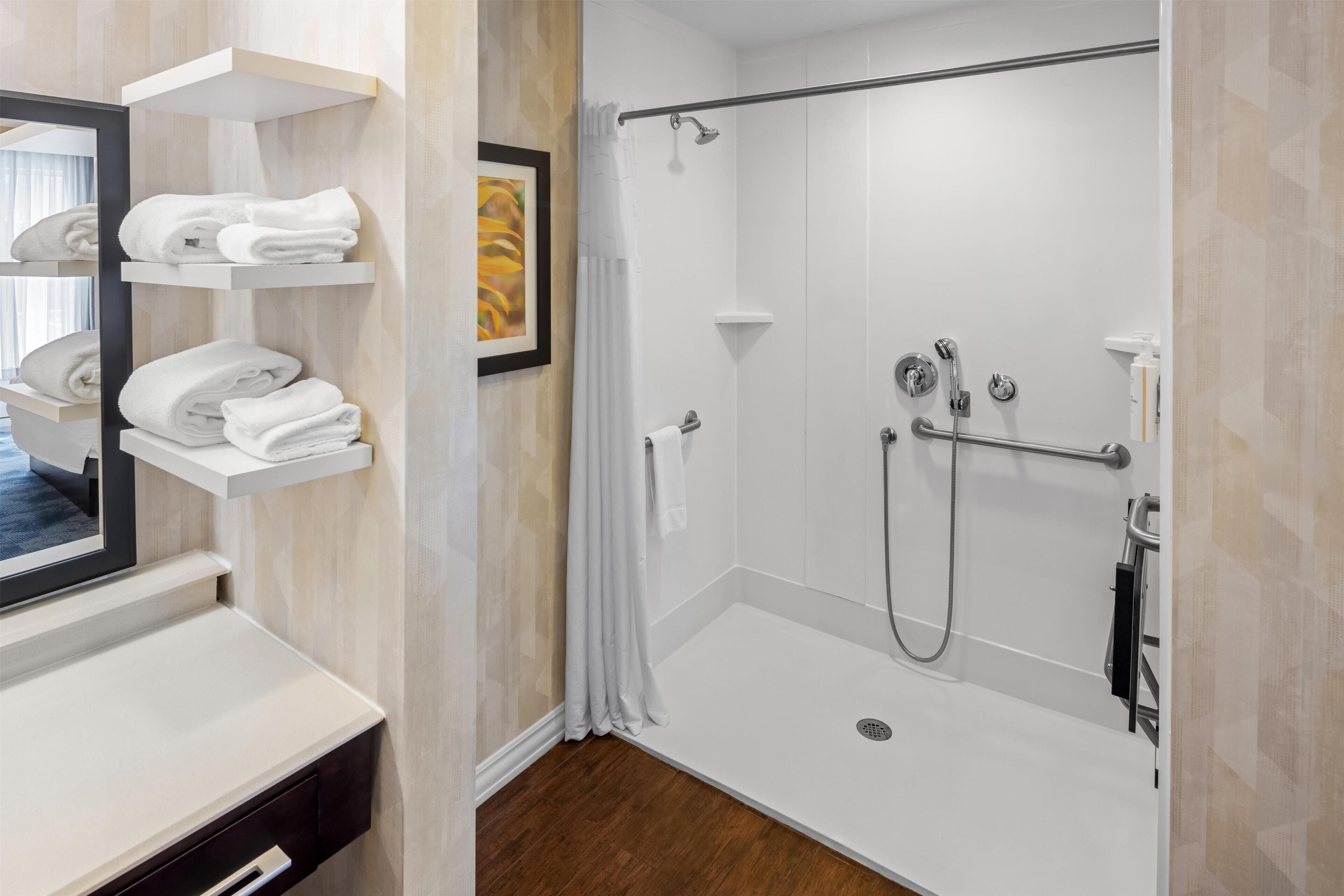 A modern bathroom with a glass-enclosed shower, white shelves with towels, and a framed picture on the wall.
