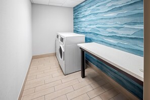 A laundry room with a washing machine, a drying rack, and a wall with a blue abstract design.