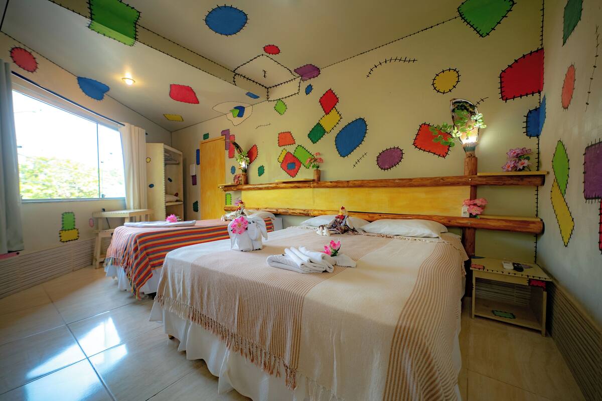 Una habitación de hotel con dos camas, un cabecero de madera, una mesita de noche pequeña y una ventana con cortinas.
