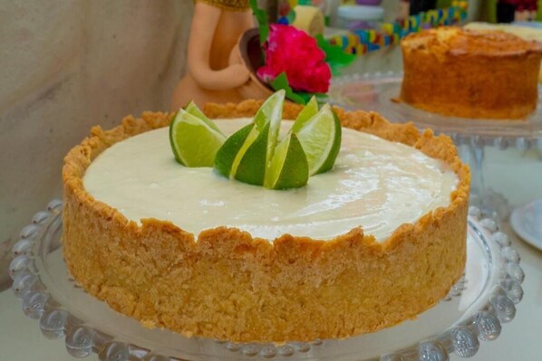 Un gâteau au fromage garni de tranches de citron vert, présenté sur un présentoir en verre transparent.