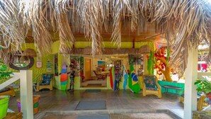 An indoor area with a thatched roof, wicker furniture, and colorful decorations including flags. - Pousada das Galinhas (Ipojuca)