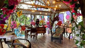 An indoor space with a wooden floor, rustic furniture, and a ceiling adorned with hanging lights and artificial flowers. - Pousada das Galinhas (Ipojuca)