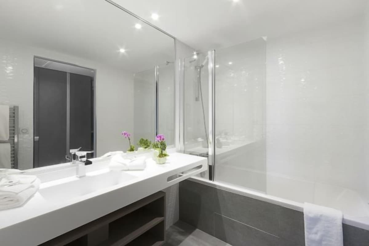 A modern bathroom with a large mirror, white vanity, and a glass-enclosed shower area.