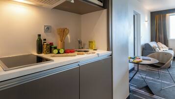 A modern kitchen with a built-in stove, a microwave, and a sink. There are fresh fruits and vegetables on the counter, and a small table with a chair.