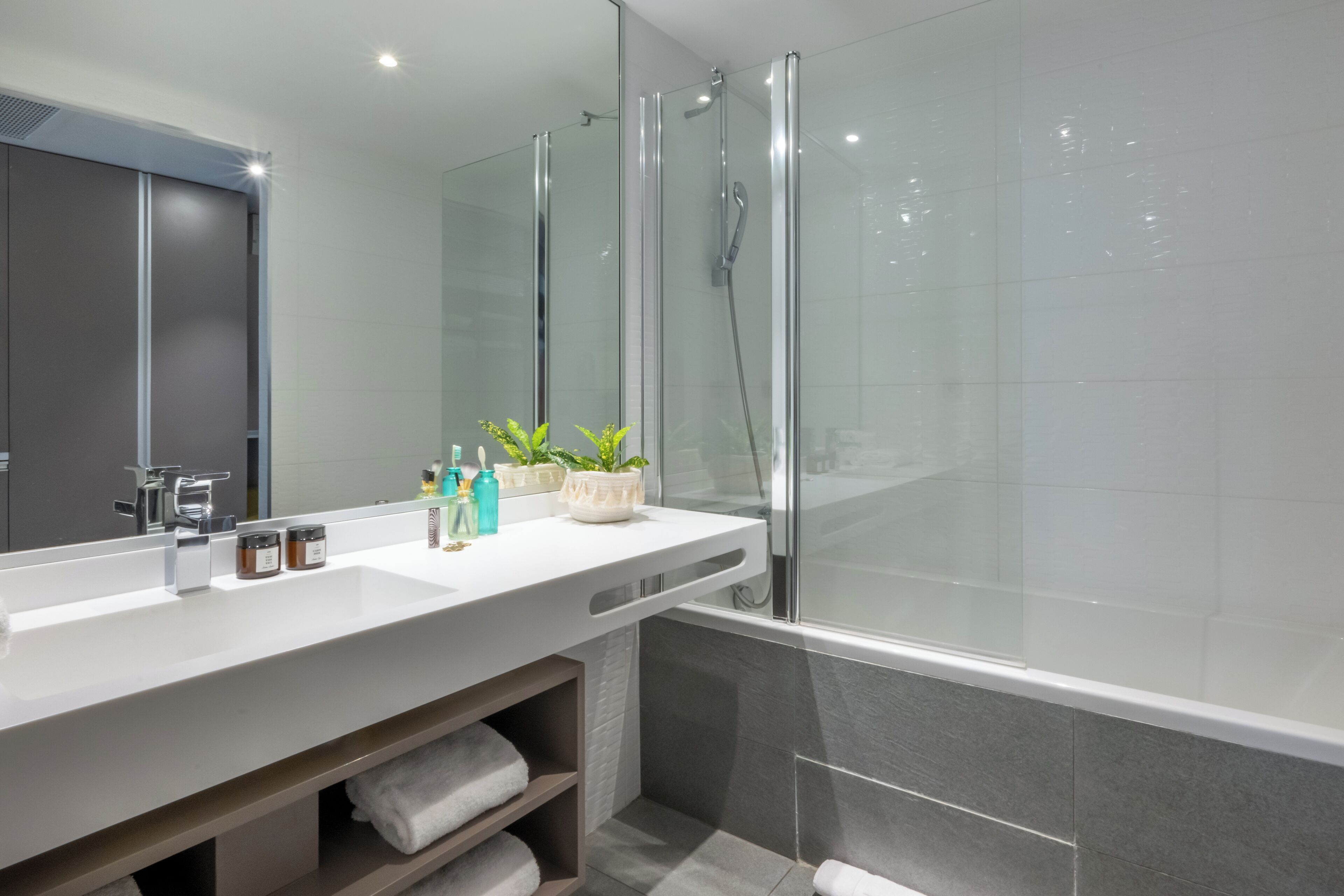 A modern bathroom with a large mirror, a white sink, and a glass-enclosed shower.