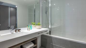 A modern bathroom with a large mirror, a white sink, and a glass-enclosed shower.