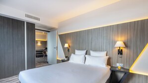 A modern hotel room with a large bed, two bedside lamps, a small table with a lamp, and a mirror. - Nemea Appart Hotel Concorde Toulouse Gare Matabiau (Toulouse)