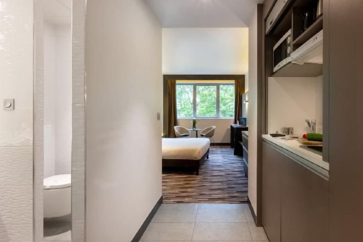 A hotel room with a bed, a small table, and a window.