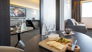 A dining area with a wooden table, cheese, pickles, and a knife. There are wine glasses and a bowl on the table. - Nemea Appart Hotel Concorde Toulouse Gare Matabiau (Toulouse)