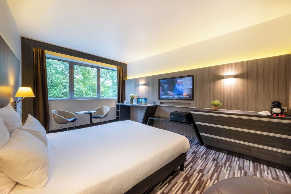 Habitación de hotel con una cama grande, un escritorio con computadora, televisión y ventana con cortinas.