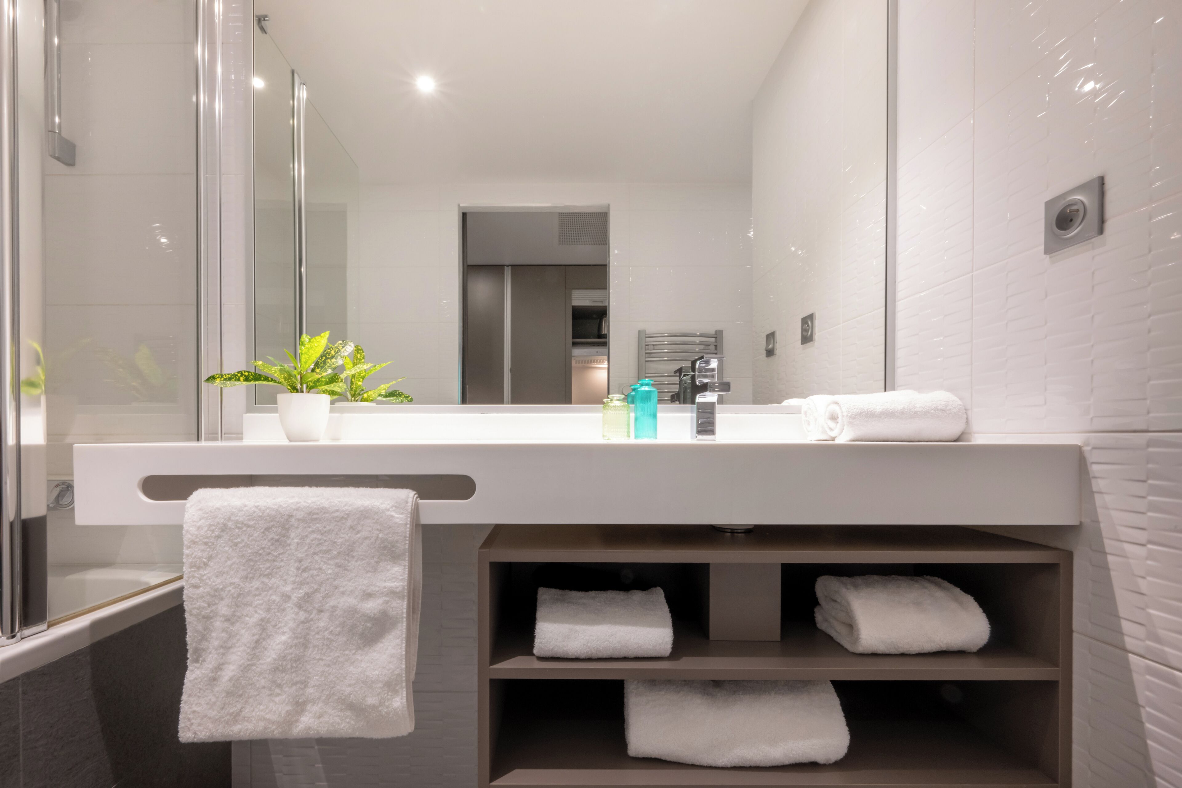A modern bathroom with a glass shower enclosure, a white sink with a mirror above it, and a towel rack with folded towels.