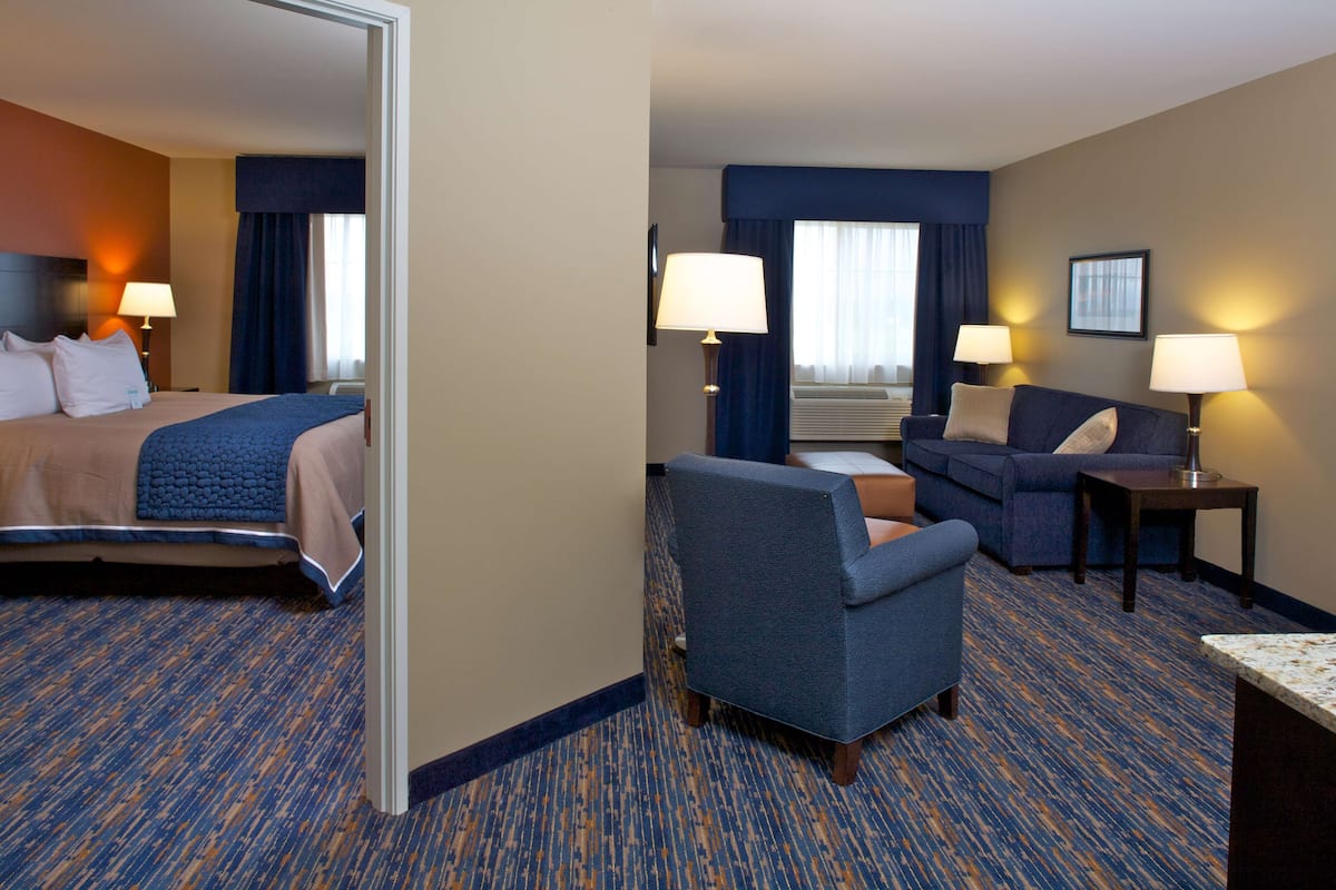 A hotel room with a bed, a sofa, a chair, two lamps, and a window with curtains.