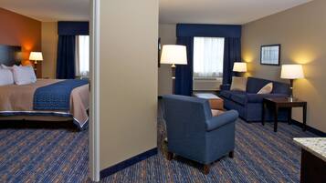 A hotel room with a bed, a sofa, a chair, two lamps, and a window with curtains.