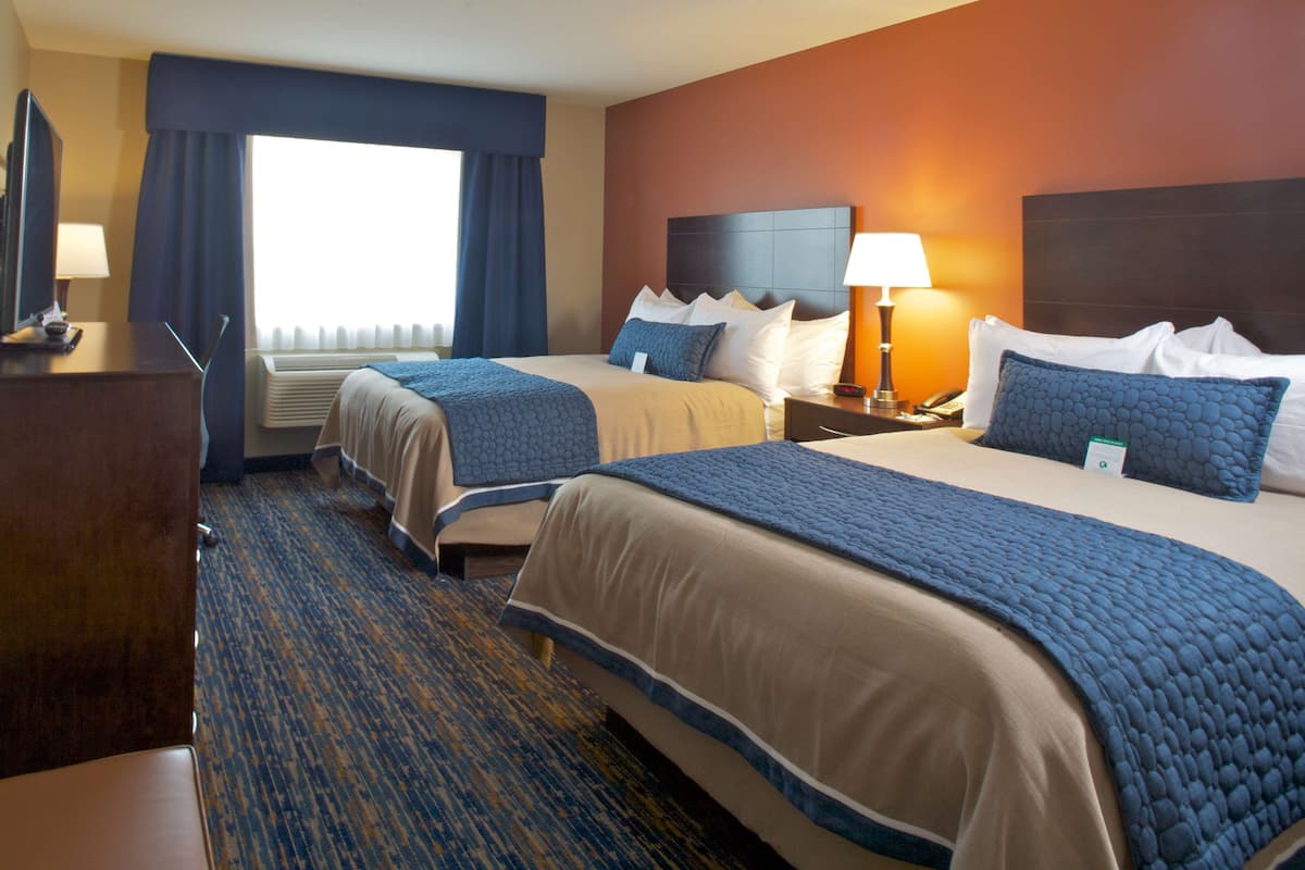 A hotel room with two beds, a desk, a TV, and a window with curtains.