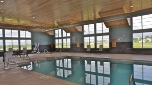 Una piscina interior con vistas despejadas al exterior gracias a amplios ventanales, techo de madera y suelo de baldosas.