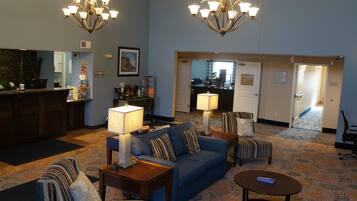 A hotel lobby with a blue sofa, striped armchairs, a wooden coffee table, and a chandelier.