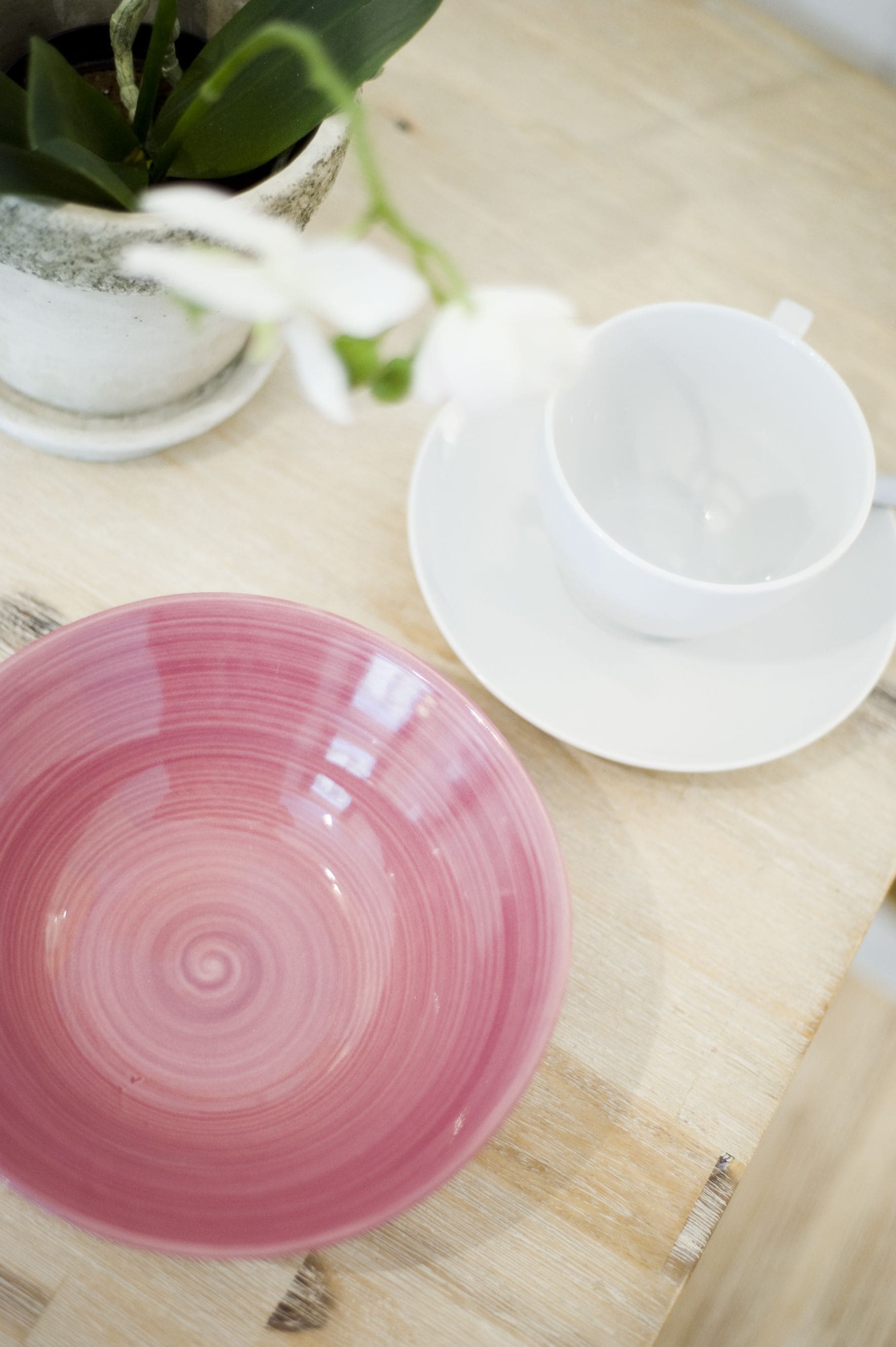 A wooden table with a pink plate, a white cup, and a white saucer.