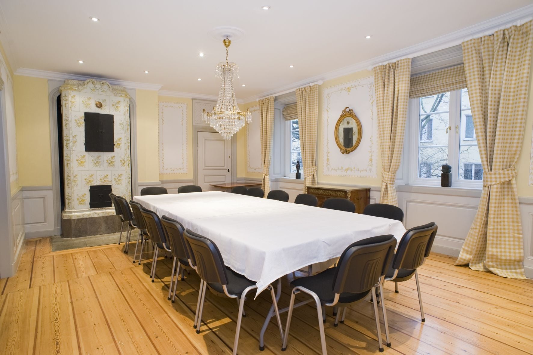A formal dining room with a long table, chairs, a chandelier, and checkered curtains.