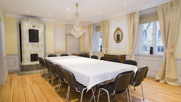 A formal dining room with a long table, chairs, a chandelier, and checkered curtains.