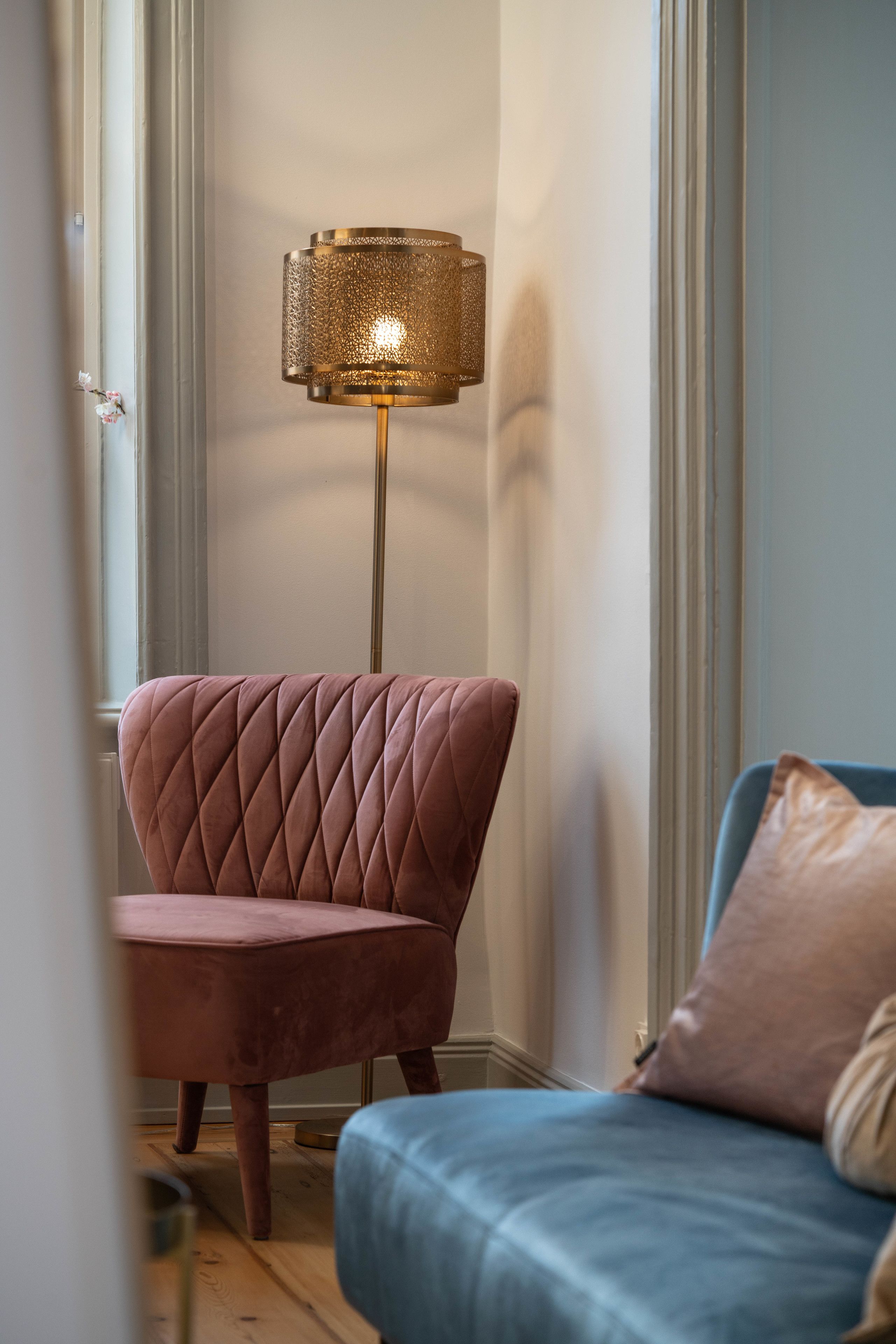 Ein Zimmer mit einem rosa gepolsterten Sessel, einem blauen Sofa und einer Stehlampe.