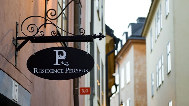 Vista de la calle con un edificio que muestra un cartel con la inscripción 'Residence Perseus'.