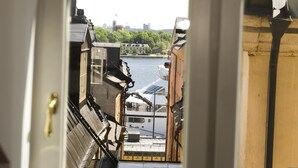 Vista a través de una ventana con marco blanco, que da a un río con edificios y un barco atracado en la orilla.