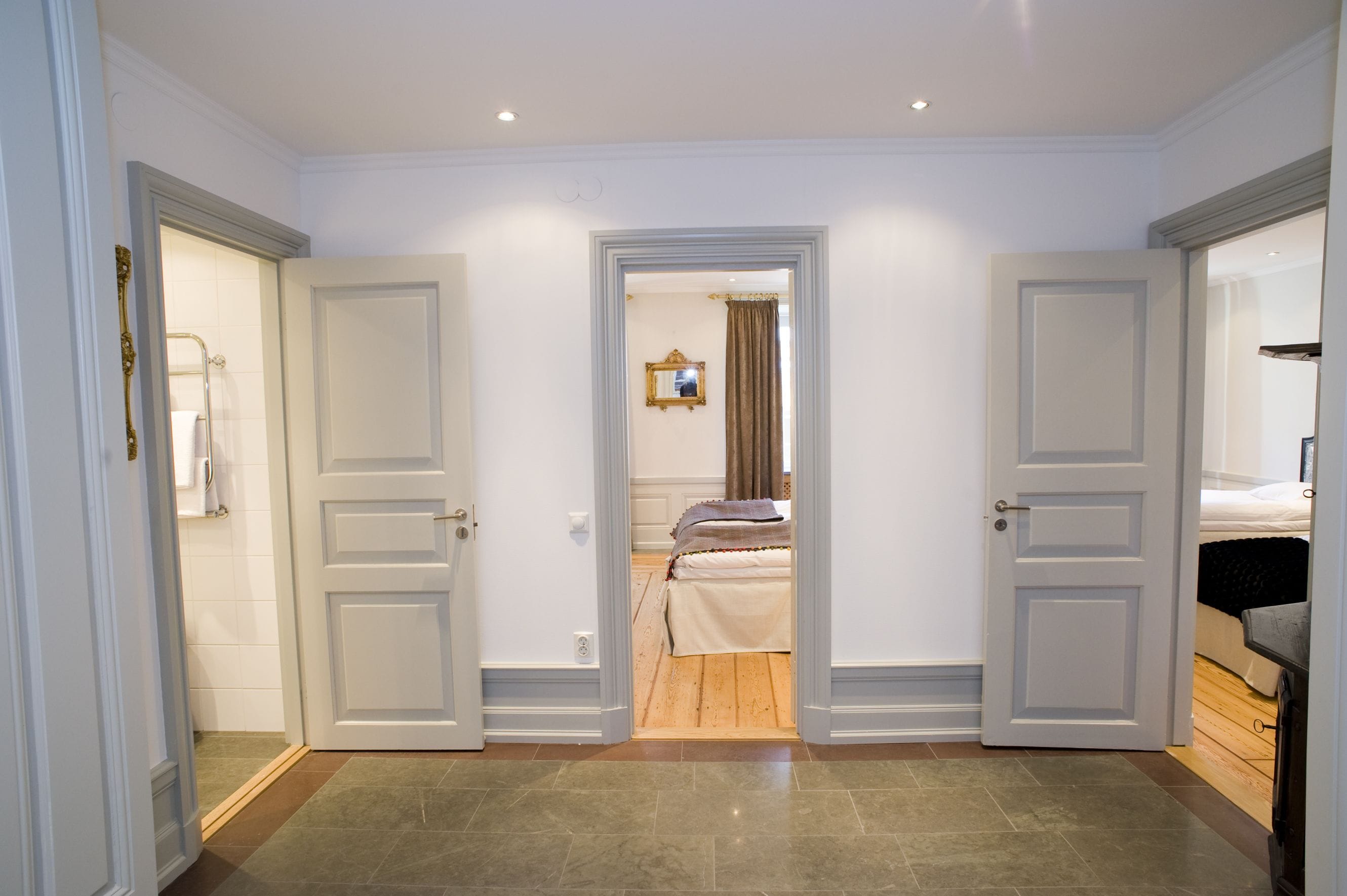 A hotel room with a wooden floor, a bed, a bathroom with a towel rack, and a mirror on the wall.