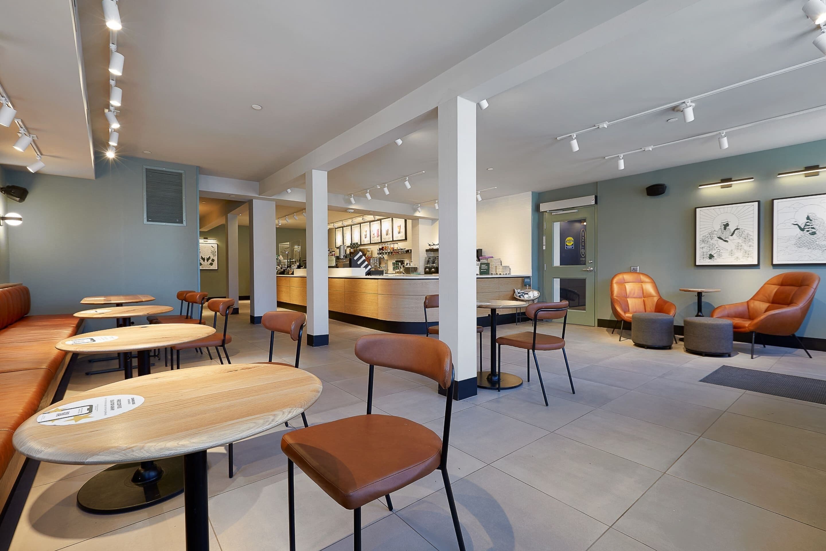 A modern cafe with wooden tables and brown chairs, a bar area, and framed artwork on the walls.