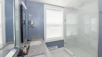 Un baño moderno con cabina de ducha de vidrio, tocador con espejo y ventana con persianas.