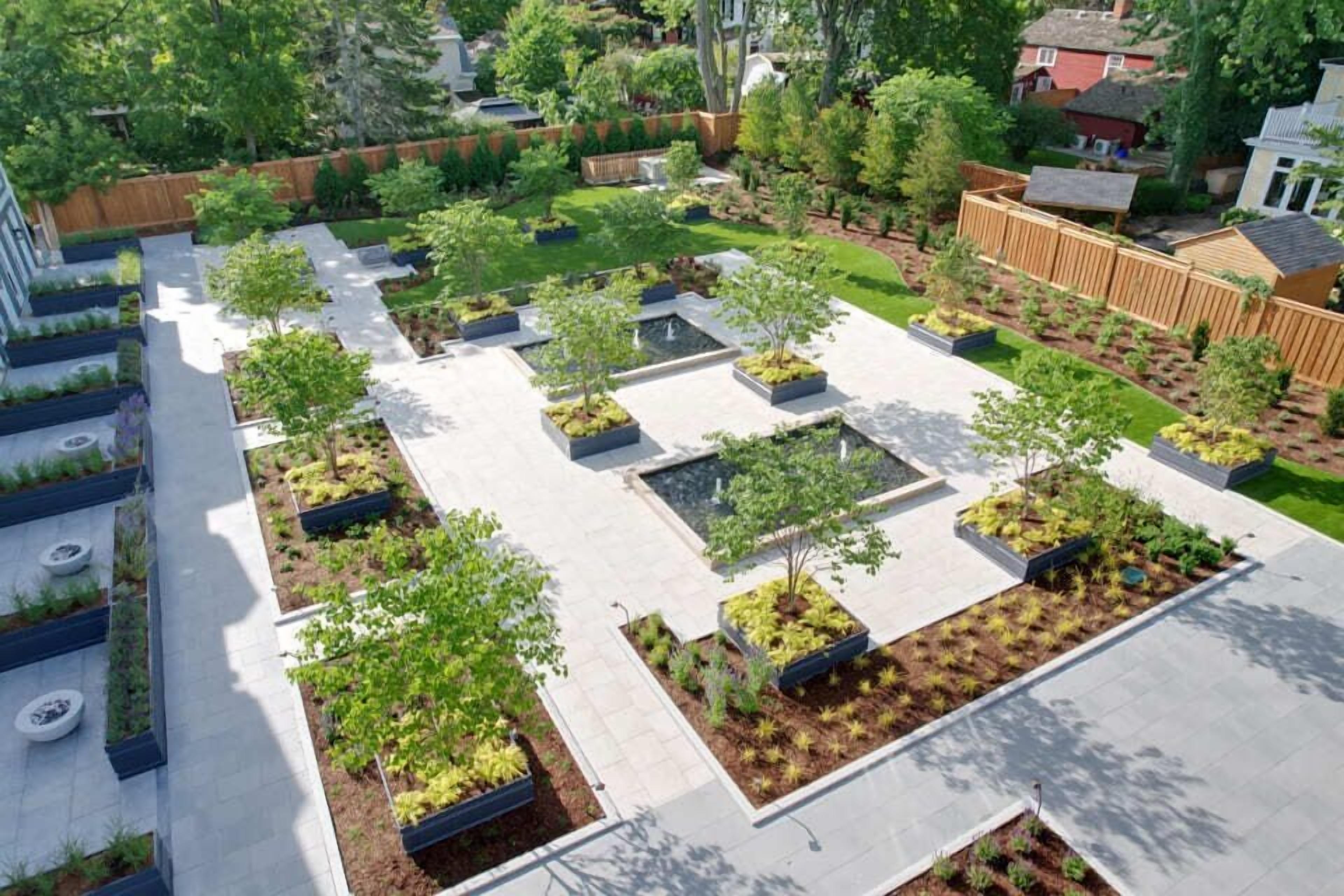 A rooftop garden with multiple planters and trees, surrounded by a paved area and a wooden fence.
