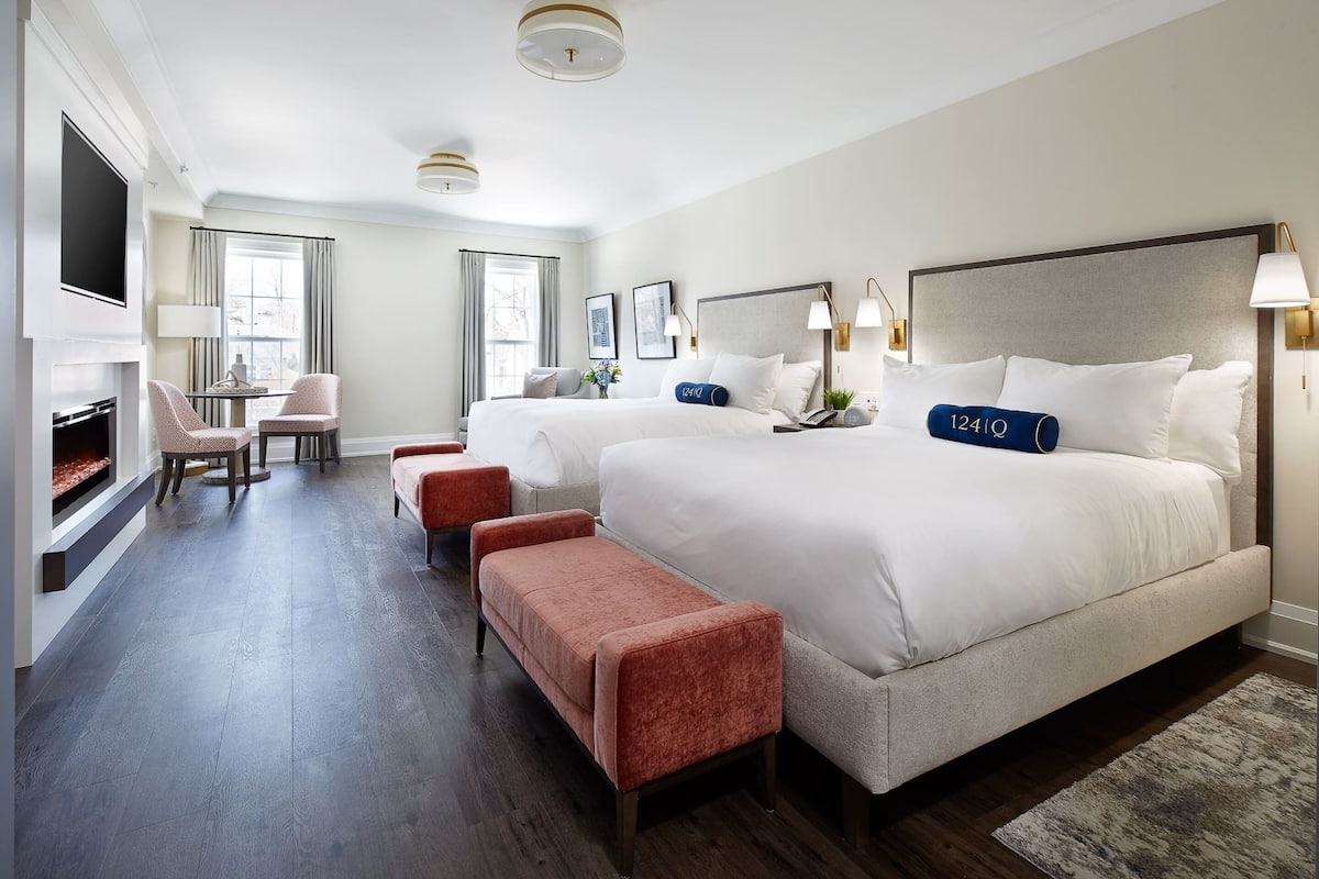 Une chambre d’hôtel avec deux lits, un coin salon avec des fauteuils, une cheminée et un téléviseur.