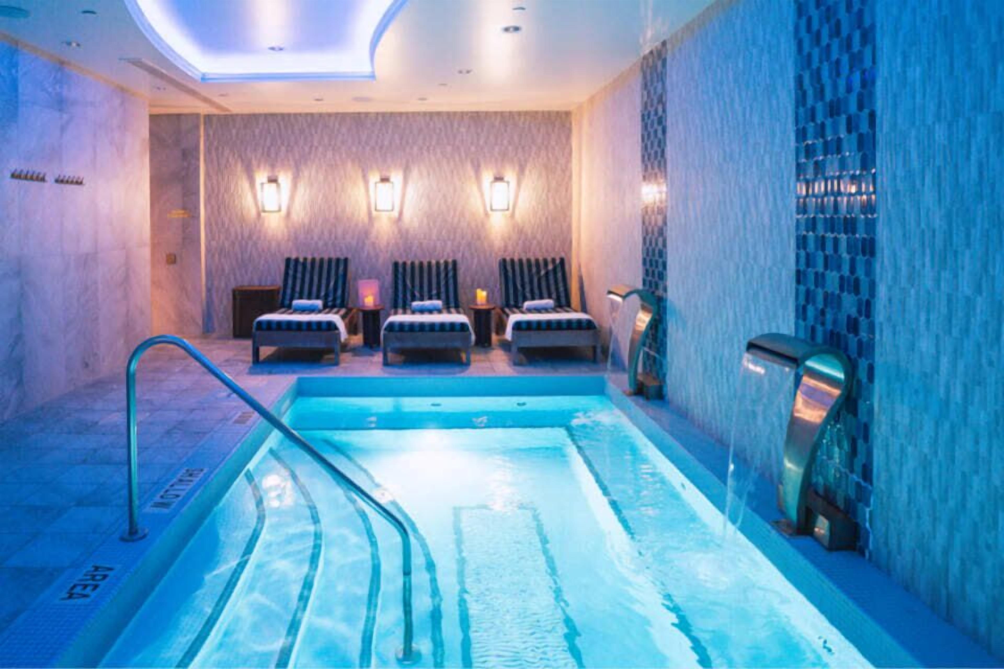 Un cuarto de spa con una piscina, tres sillas de masaje e iluminación empotrada.