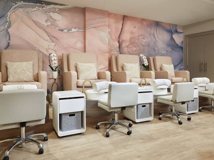 Un salón con varias sillas de tratamiento, un gran mural en la pared y un armario con toallas.