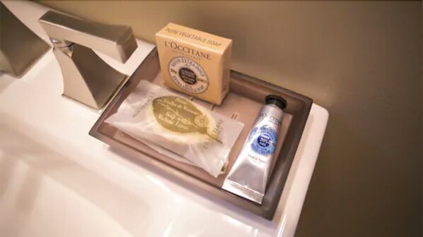 A tray with a bar of soap, a small packet, and a tube of cream on a bathroom sink.