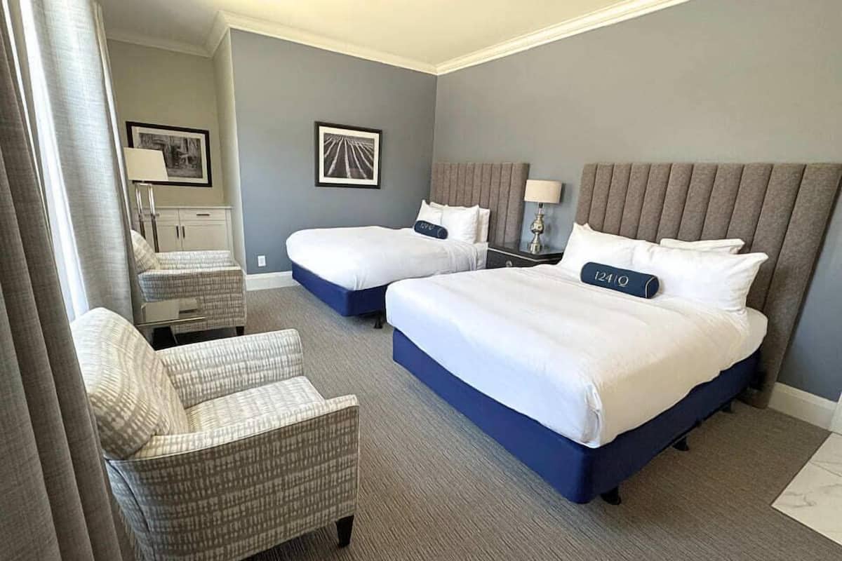 Une chambre d’hôtel avec deux lits, une chaise, une table de chevet et une lampe.