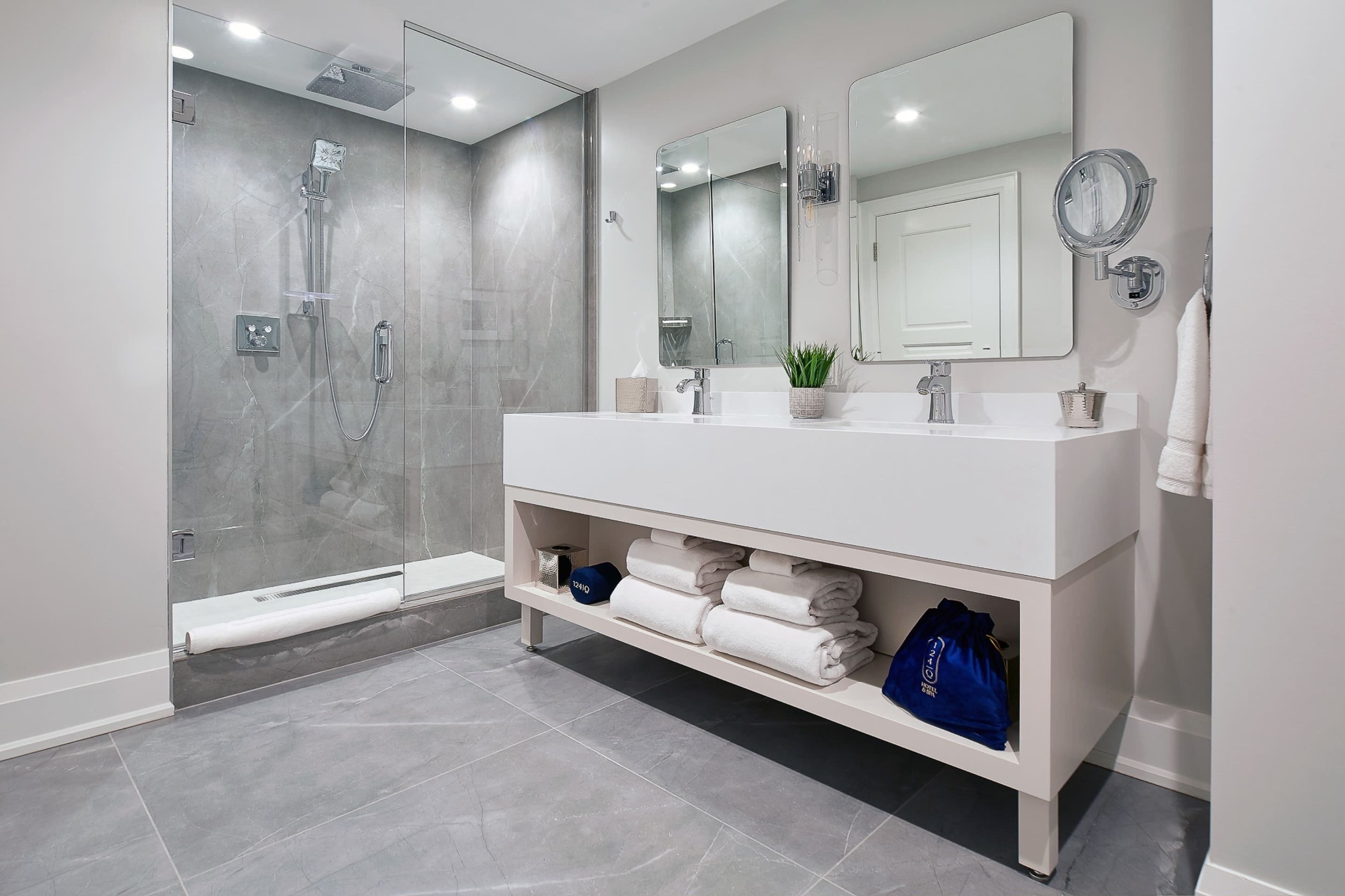 Un baño moderno con ducha envuelta en vidrio, un tocador blanco con espejo y toallas dobladas con cuidado.