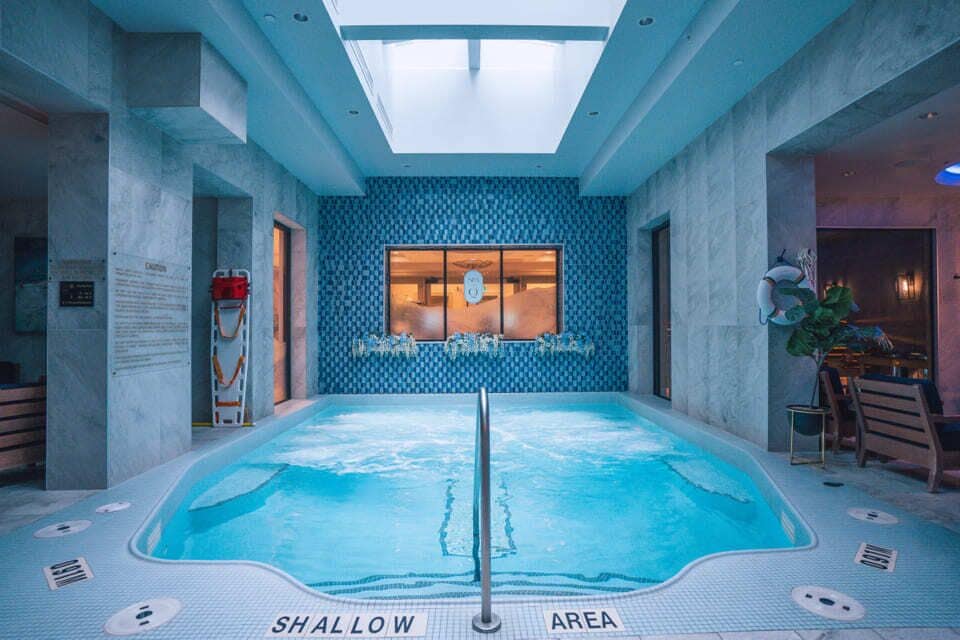 An indoor swimming pool with a skylight, a shallow area, and a view of a bar area.