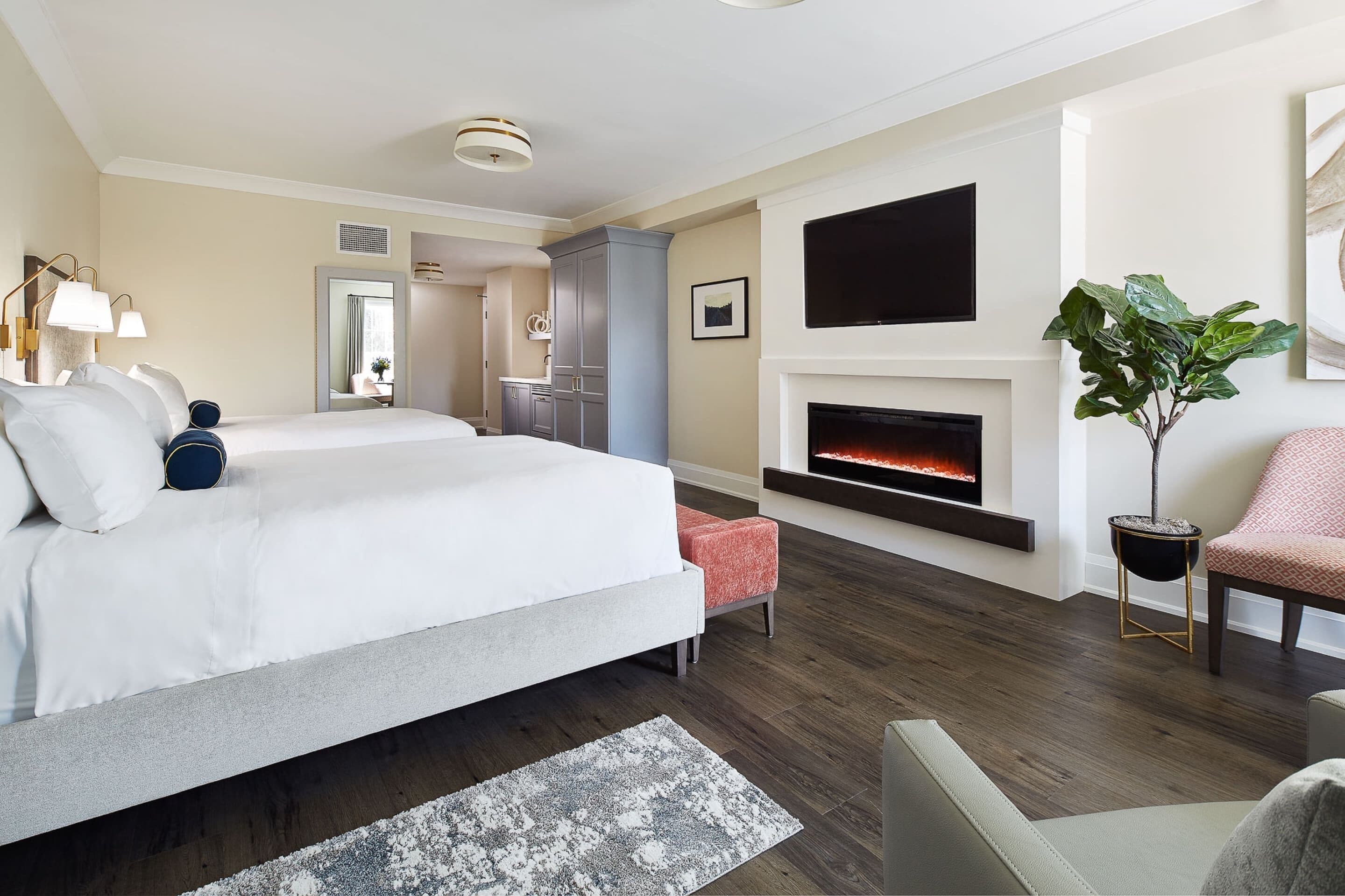 A modern hotel room with a large bed, a fireplace, a TV, and a seating area with a plant.