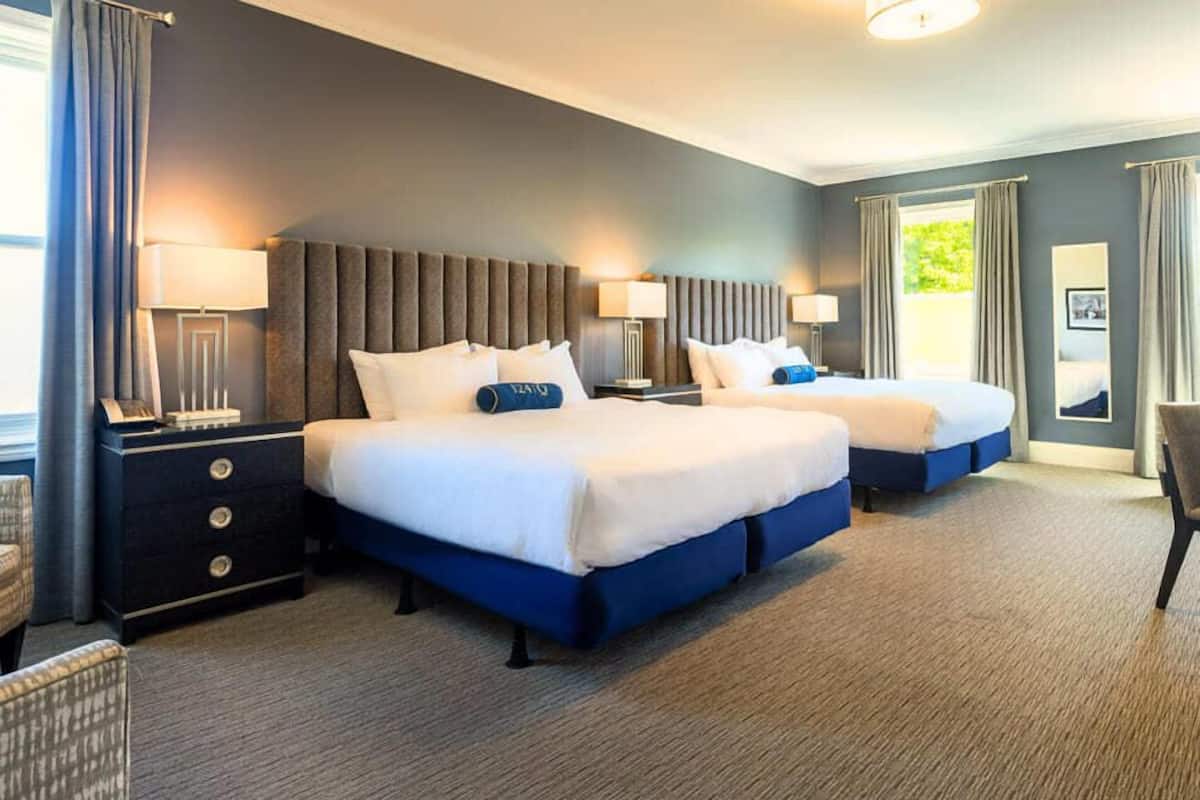 Une chambre d’hôtel avec deux lits, une table de chevet, une chaise et une fenêtre avec des rideaux.