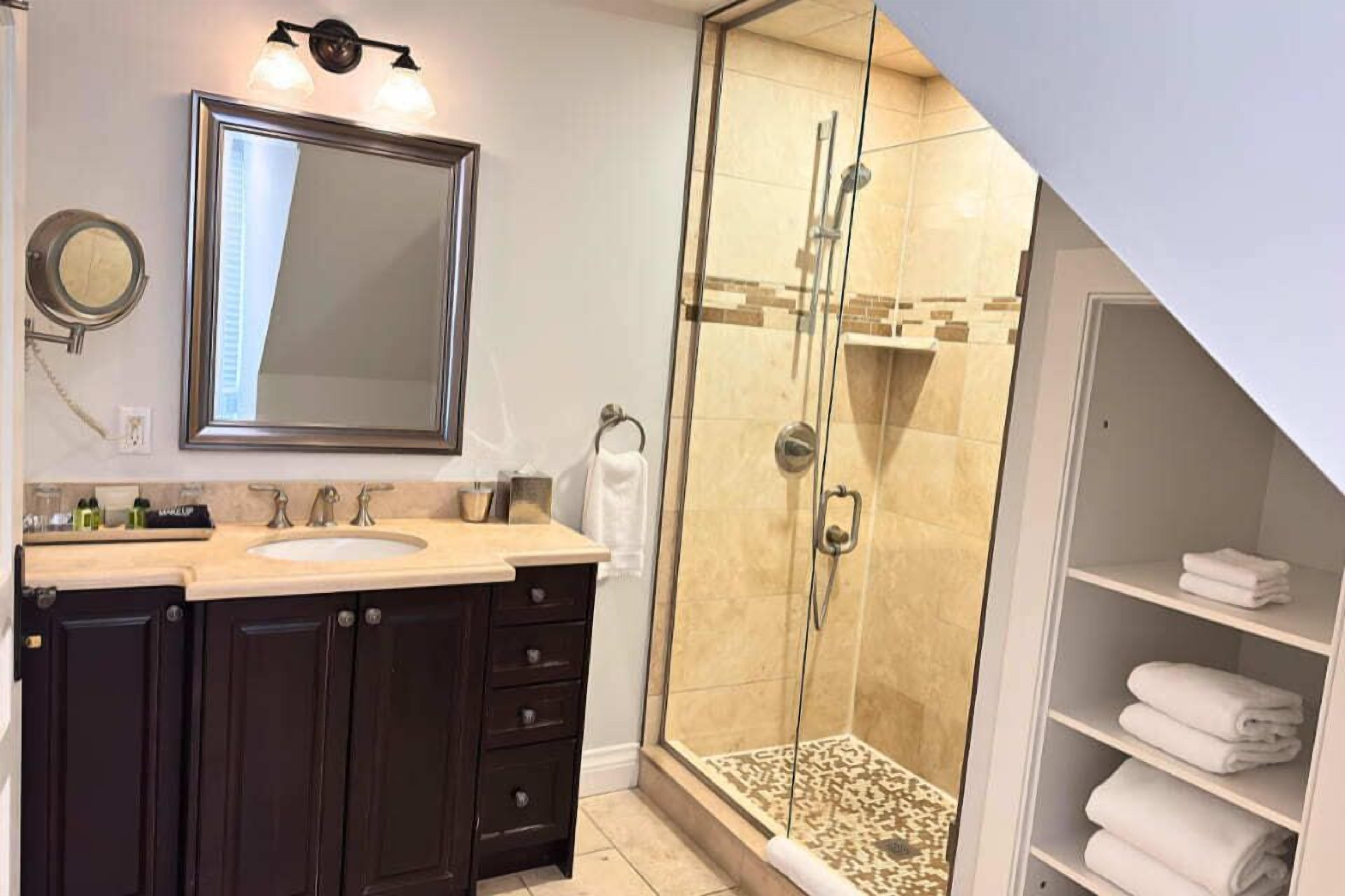 A bathroom with a large mirror, dark cabinets, a sink, and a glass-enclosed shower area.