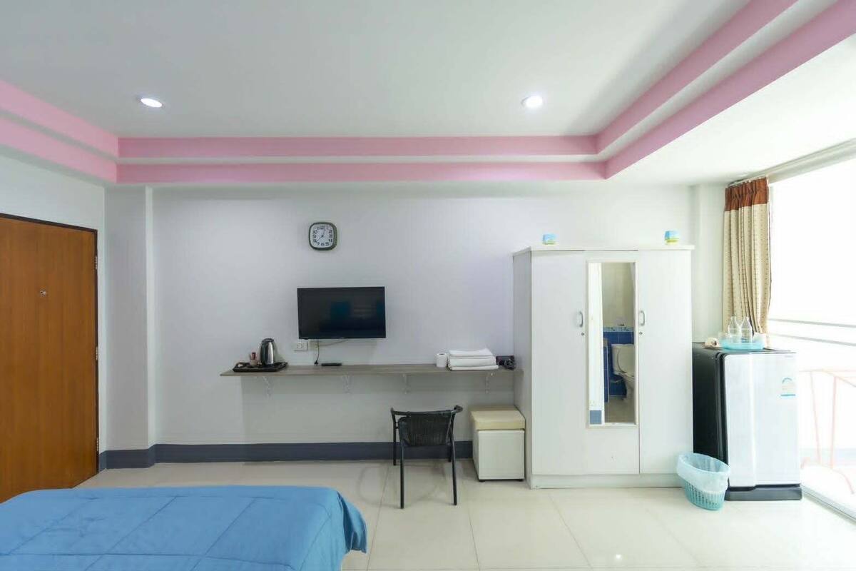 Un dormitorio con cama, escritorio, televisor, armario y ventana con cortinas.