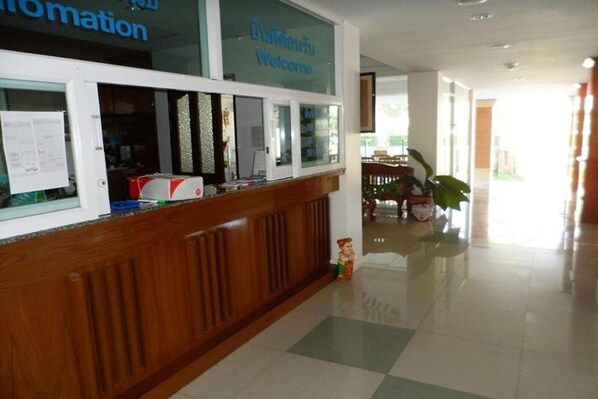 A reception desk with a wooden panel design, a glass partition with a welcome sign, and a small plant on the floor. - Kaewchantra Mansion (Chiang Mai)