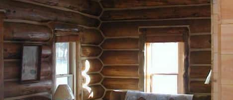 A log cabin interior with a sofa, armchair, lamp, and a refrigerator.