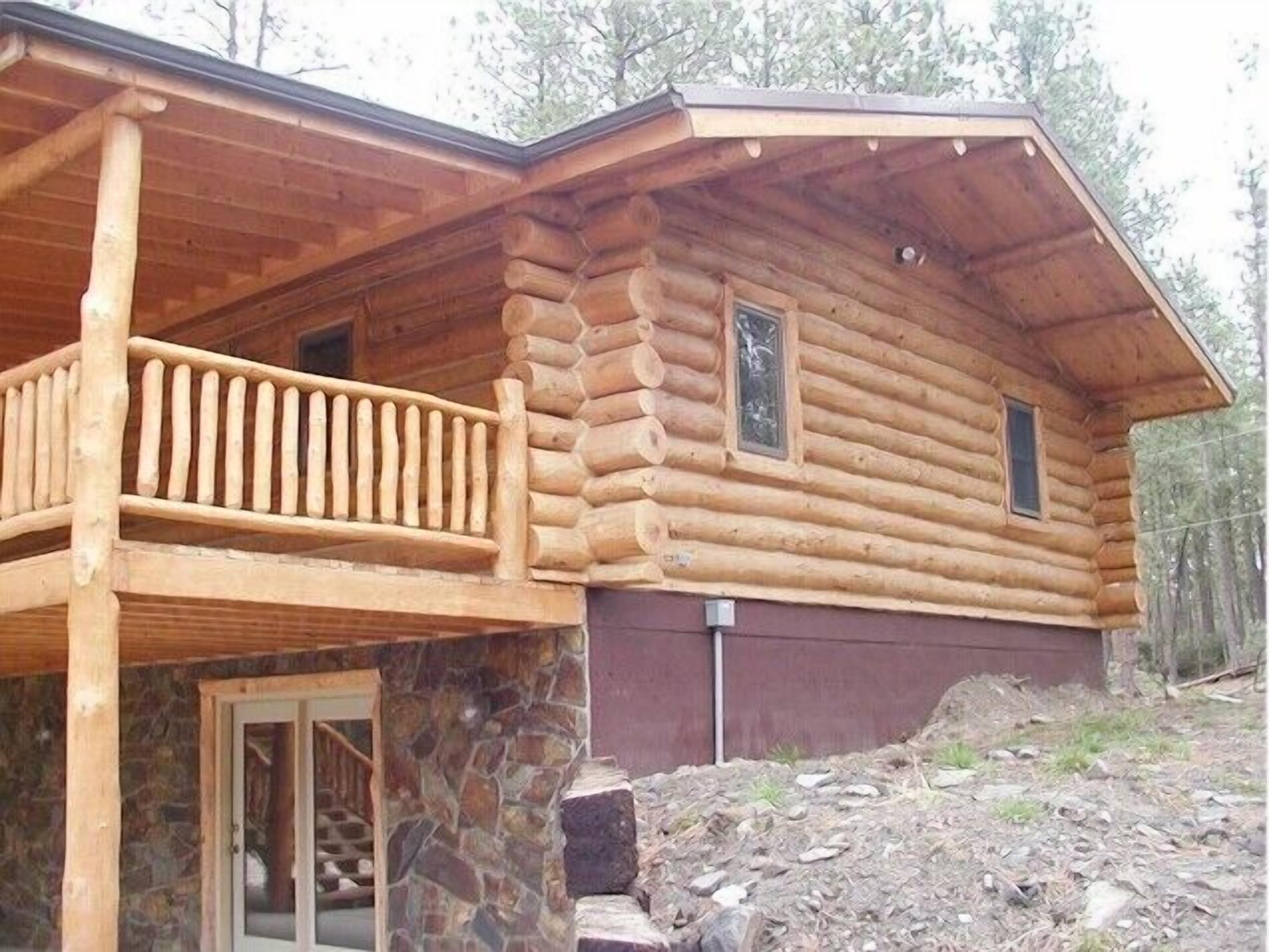 A log cabin with a stone foundation, a wooden balcony, and a stone wall.